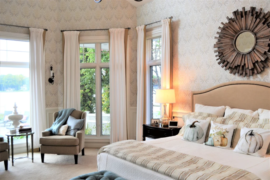 Elegant bedroom with large windows, neutral palette, soft lighting, and cozy seating, creating a tranquil and inviting space.